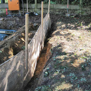 Um ein Wegrutschen des Substrates in die Grube zu verhindern, wird eine Seite mit Pfählen, Stahlgittern und Ballentuch gesichert (Wurzelvorhang).